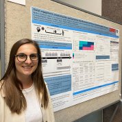 Woman wearing glasses poses with her research poster