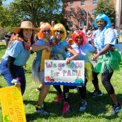 A group of NIH'ers wearing colorful wigs pose together with a sign reading We go Coco for PACU
