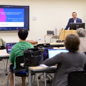 Meerzaman at lectern with students at desks in foreground
