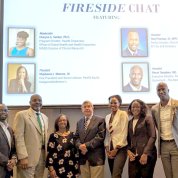Seven people stand in front of chat title slide projected on screen