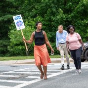 Three people crossing at crosswalk with the woman in front holding up a NINDS sign