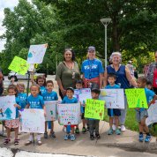 A big group of preschool kids holding signs gathers.