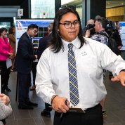 Woman stands viewing a poster as a young man in shirt & tie gestures toward it.