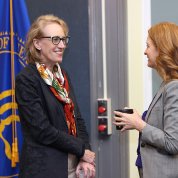 Two women stand talking to each other, each holding a cup.