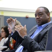A man gestures with his hands as he speaks from his seat at the conference table.