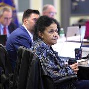 Woman seated at conference table looks at projection screen.