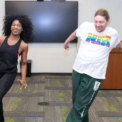 A woman and man each with one leg extended and arms up while doing cardio