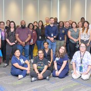 Large group of people, some standing, some seated, in conference room