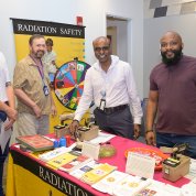 A group of guys at table with Radiation Safety sign and a colorful wheel game to teach safety tips