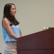 Szwec, wearing a light blue shirt, speaks at a lectern.