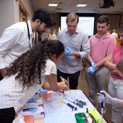 People wear surgical gloves and use pipettes to put liquid into test tubes.