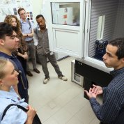 A group of people listen to a person while looking at a complex piece of research equipment inside a soundproof box.