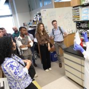 A person is showing a small vial and diagram to a group of people in a lab. 