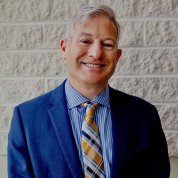 A smiling Goldstein stands in front of an off-white brick wall.