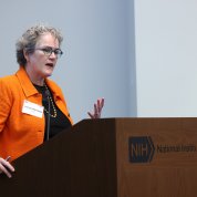 Marrazzo, wearing a bright orange jacket, speaks at a lectern.
