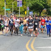 A group of runners race down a street as cheering onlookers fill the sidewalk.