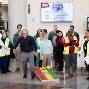 Perez-Stable holds beanbag, next to a cornhole board, surrounded by colleagues in the CC atrium.