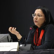 Zaidi, seated, speaks into a microphone and gestures with her right hand.