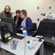 Woman at computer monitor gestures toward screen as man and two other women look on.