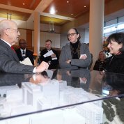 Man gestures toward architectural model of building, as two women observe