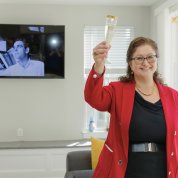 Smiling woman holds up glass flute with screen projecting photo of Phil Leder behind her