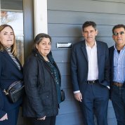 Two women and two men stand outside doorway of house, with plaque showing name Phil Leder House