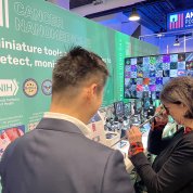 Bertagnolli peers into the eyepiece of a long, thin instrument. A scientist whose back is to the camera looks on.