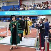 Wide view of arena with title banners in background and the faculty procession in foreground.