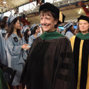 Bertagnolli, in graduation regalia, smiles ahead of Armstrong with graduates and guests looking on