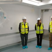 Three men in yellow vests and construction hats stand in operating room.