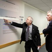 Green points at a poster featuring DNA informationas McAuliffe looks on