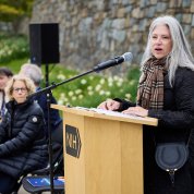Woman with long gray hair speaks at a podium.
