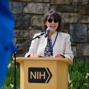 Bertagnolli, wearing dark glasses, speaks into a microphone at a lectern.