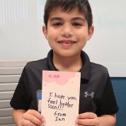 A smiling child holds up a card he made that reads: "I hope you feel better soon" at the Children's Inn.