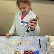 A child holds pipette and puts colorful liquid into vials.