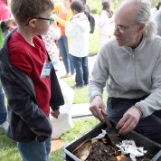 A child listens to an NIH'er talk about composting, as he holds a bucket of soil, food scraps and worms under the tent in front of Bldg. 1.