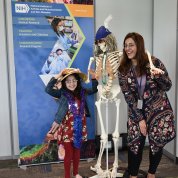 Mom and daughter pose, smiling, next to skeleton Mr. Bones.