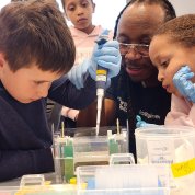 Dr. Platt guide's child's hand as he pipettes over a tray and other kids look on.