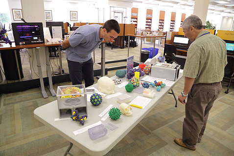 Two men browse a table display of various inventions 