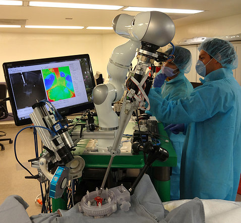 Surgeons look at colorful computer screen display surgical robot making stitches in tissue.