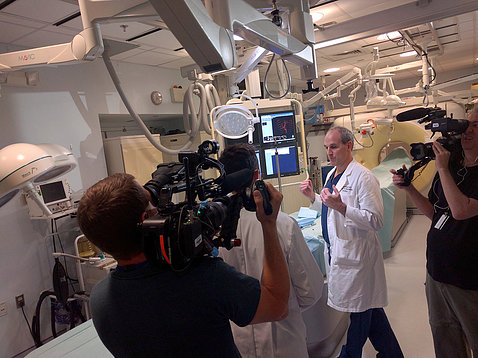 A TV cameraman points video camera at Dr. Wood in a testing room in the Clinical Center