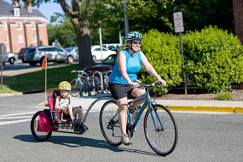Bicyclist pedals bike towing a child in carrier attachment.