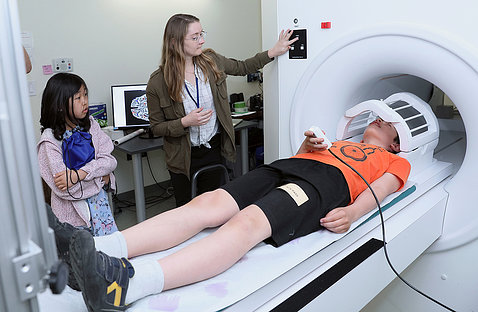 A boy lays on his back in MRI scanner, as postbac fellow talks him through the exercise.