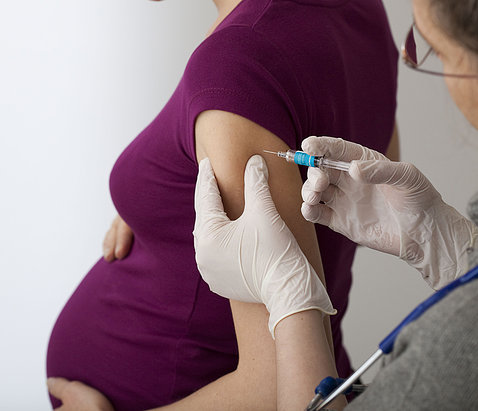 A lab tech inserts needle into arm of pregnant woman 