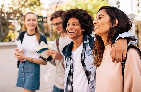 Four smiling teens walk arm-in-arm down the street.