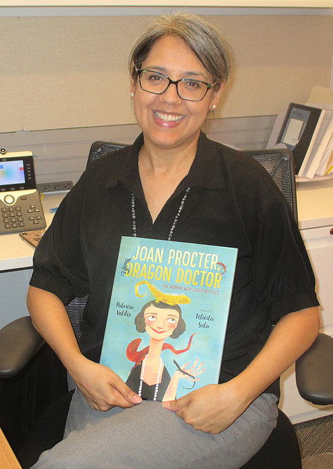 NIH's Dr. Patricia Valdez sits in her office, smiling, holding up a copy of her book.