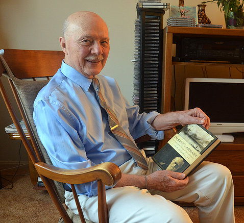 Dr. Remondini in his home, sitting in a rocking chair holding a book