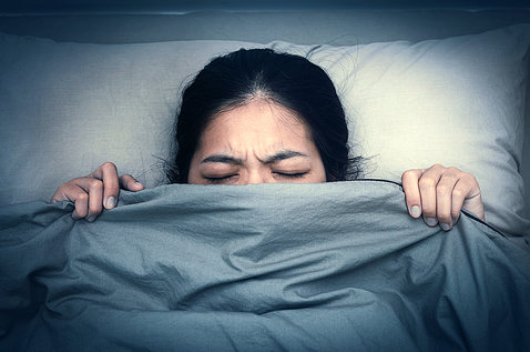 A woman in bed pulls her blanket up past her nose