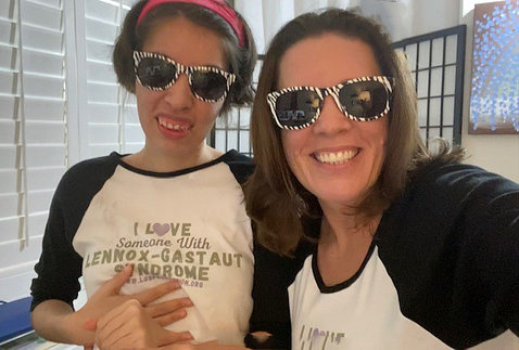 A smiling young Savannah in an "I Love Someone with Lennox-Gastaut syndrome" shirt, with her smiling mom; both are wearing sunglasses.