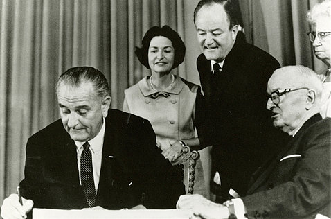 Johnson signs a paper, with four people looking on.